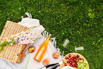 leisure and drinks concept - close up of food, drinks and basket on picnic blanket on grass
