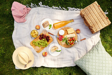 leisure and eating concept - close up of food, drinks and picnic basket on blanket on grass at...