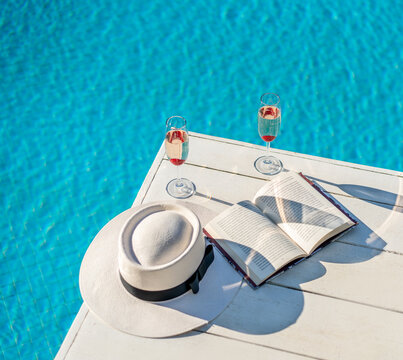 Exotic refreshing cocktails by the pool with book and straw hat.