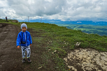 A little boy against the background of the mountains and the Bermamyt plateau in Russia. June 2021