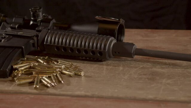 Wide dolly in of AR-15 with a lot of ammunition lying on wooden surface