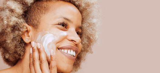 Close up portrait of young cheerful afro latin american woman with moisturizer on face. Facial mask...