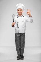 cooking, culinary and profession concept - happy smiling little boy in chef's toque and jacket with whisk showing ok gesture over grey background
