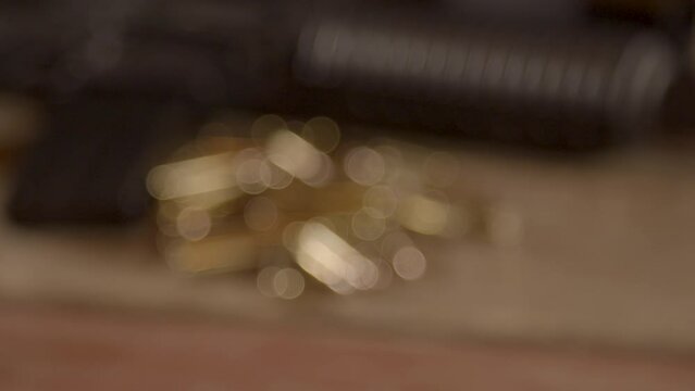 Close dolly out of a lot of ammunition lying in front of AR-15 rifle. Shot starting out of focus and slowly getting into focus