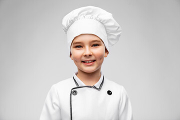 cooking, culinary and profession concept - portrait of happy smiling little boy in chef's toque and jacket over grey background