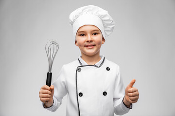 cooking, culinary and profession concept - happy smiling little boy in chef's toque and jacket with whisk showing thumbs up over grey background