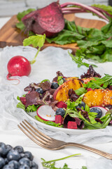 Fresh spring salad with rucola, lettuce, blueberries, radish, beet and slices of peach. White background with free text space