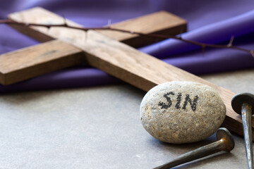 Stone with word sin, nails and wooden cross on violet fabric. Christ crucifixion for sins of people concept 