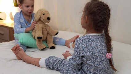 Two Smiling Preschool Toddler Children In Pajamas Playing With Teddy Bear on Bed. Siblings Little Twins Boy and Girl Have Fun. Happy Kids On Quarantine At Home. Friendship, Family, Education Concept - Powered by Adobe