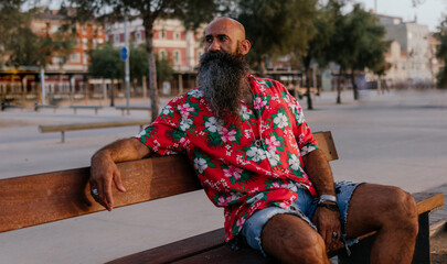 Portrait of a Bearded man dressed in hawaiian shirt sitting on a bench of a city street looking away thoughtful © anuatmoralesfoto