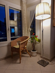 Home decor. Cozy corner with wicker armchair, potted flowers and lighted lamp.