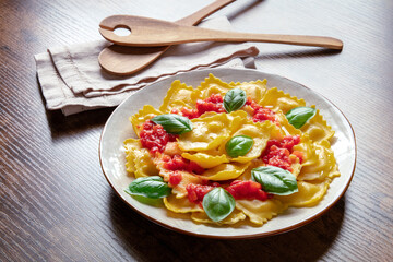 Ravioli with tomato sauce and fresh basil leaves. Italian recipe on a rustic wooden background