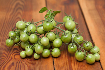 A bunch of unripe, green, cherry tomatoes lying on a wooden table top.