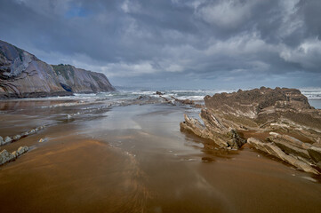 Preciosa playa de Zumaia cuando sube la marea bajo altos acantilados y un cielo nuboso.