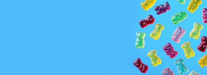 Multicolored flying gummy bears on blue background, flat lay. Banner