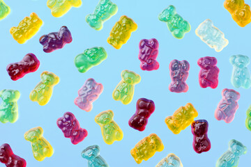 Multicolored flying gummy bears on blue background, flat lay