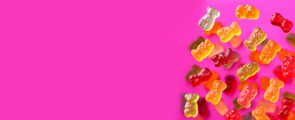 Multicolored flying gummy bears on a pink background, flat lay. Banner