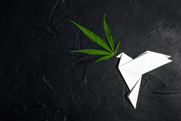 Paper origami dove of peace with green cannabis leaf on a black background with copy space.