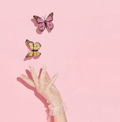 Spring creative layout with woman hand in lace glove  and colorful butterflies  on pastel pink  background. 80s, 90s retro romantic aesthetic summer concept. Minimal surreal fashion idea.