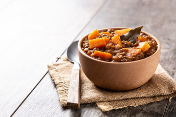 Lentil stew ragout with pumpkin and carrot in bowl on wooden table. Copy space