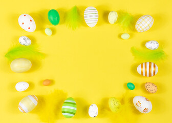 Easter frame with eggs and feathers on a yellow background. Minimal concept. View from above. Card with copy space for text.