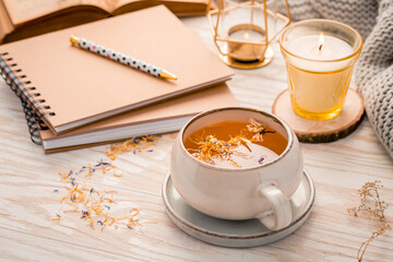 Cozy lifestyle - hot herbal tea with notepad, candle, book and blanket