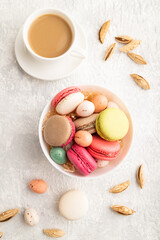 Fototapeta na wymiar Different colors macaroons and chocolate eggs in ceramic bowl, cup of coffee on gray concrete background. top view, close up.
