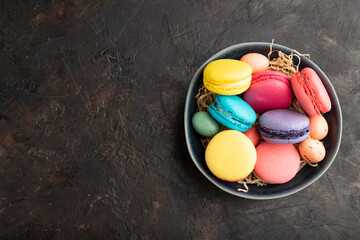 Different colors macaroons and chocolate eggs in ceramic bowl on black concrete background. top view, copy space.