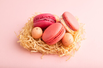 Magenta and pink macaroons and chocolate eggs in decorative paper nest on pink pastel background.  side view, close up.
