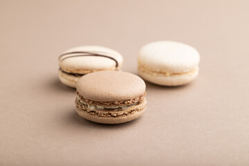 Brown and white macaroons on beige pastel background. side view, close up.