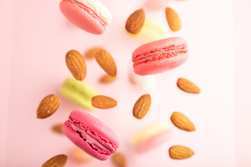 Different colors flying macaroons and almonds frozen in the air on blurred pink background. top...