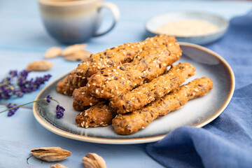 Crumble cookies with seasme and almonds on ceramic plate with cup of coffee on blue wooden background. side view, close up, selective focus.