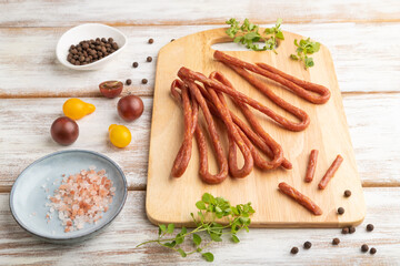 Polish smoked pork sausage kabanos on cutting board with salt and pepper on white wooden background. Side view, close up.