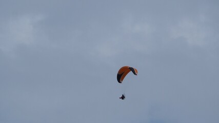 aparato de vuelo individual formado por una vela color naranja, negro y blanco y un motor guiado por un piloto, lerida, españa, europa 
