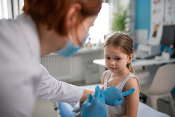 Worried little girl getting vaccinated in doctor's office. - obrazy, fototapety, plakaty
