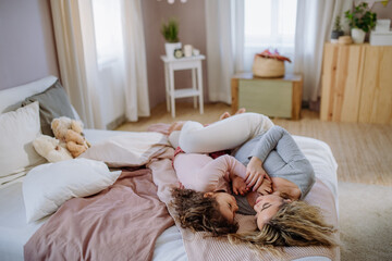 Happy mother with her little daughter lying and looking at each other together on bed at home.