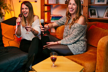 Girls with beautiful voices sit at home, drinking and sing a duet at karaoke night.