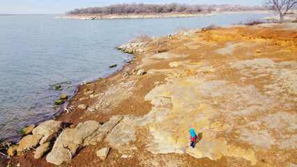 Aerial view unidentified kid wears jacket and shoes running near rocky shoreline at Grapevine Lake,...