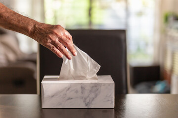 Senior man hand picking up tissue paper from tissue box on dinner table.