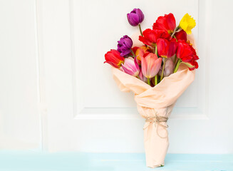 Bouquet of colorful tulips wrapped with pink paper on white wooden  background 