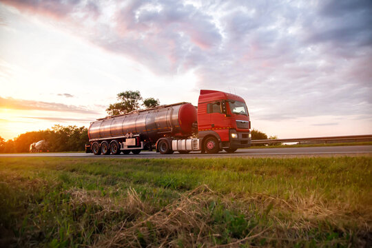 A modern truck with a semi-trailer tanker transports dangerous goods against the backdrop of a sunset in summer. Liquid cargo transportation. Copy space for text
