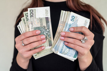 Young woman smiling happily, holding Polish zloty banknotes in the city.