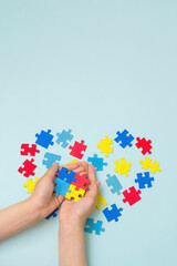 World autism awareness day. Autistic Pride Day. Hands of a small child holding colorful puzzles on blue background. Heart of puzzles.