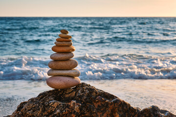 Fototapeta na wymiar Concept of balance and harmony. Cairn stack of stones pebbles cairn on the beach coast of the sea in the nature on sunset. Meditative art of stone stacking