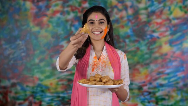 An Indian woman offers traditional Gujiya to her guests on the festival of Holi - sweet delicacy  a tasty cuisine. A young smiling woman with a Gulal Tilak on her forehead happily posing for the ca...