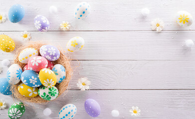 Happy easter! colourful Easter eggs in a nest with flower on white wooden background.