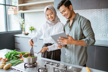 muslim couple cooking together in the kitchen while look at video