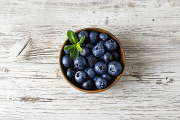 Fresh ripe blueberries in a wooden bowl. Mint leaves on berries. Top view, space for text