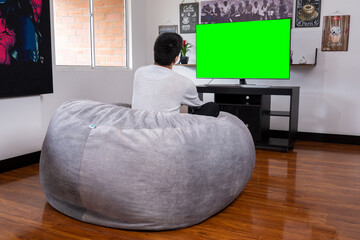 Hombre latino viendo tv en un puff - obrazy, fototapety, plakaty