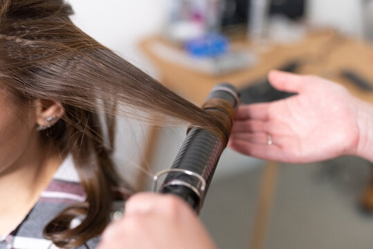 The stylist curls the girl's hair with a curling iron